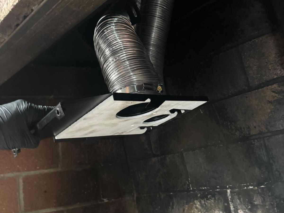 Gloved hand fitting an adapter plate connected to two stainless steel flexible liners inside a fireplace