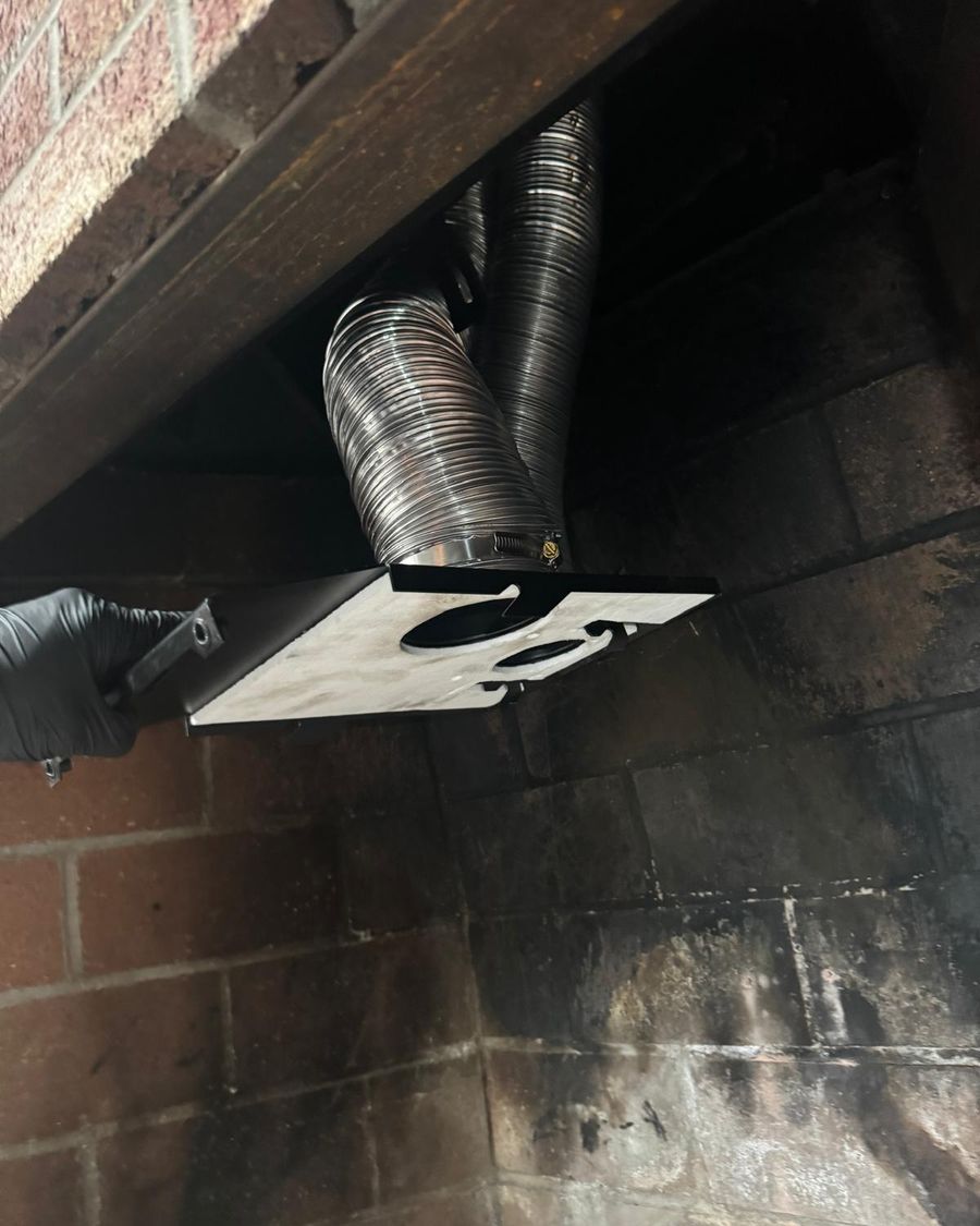 Gloved hand fitting an adapter plate connected to two stainless steel flexible liners inside a fireplace
