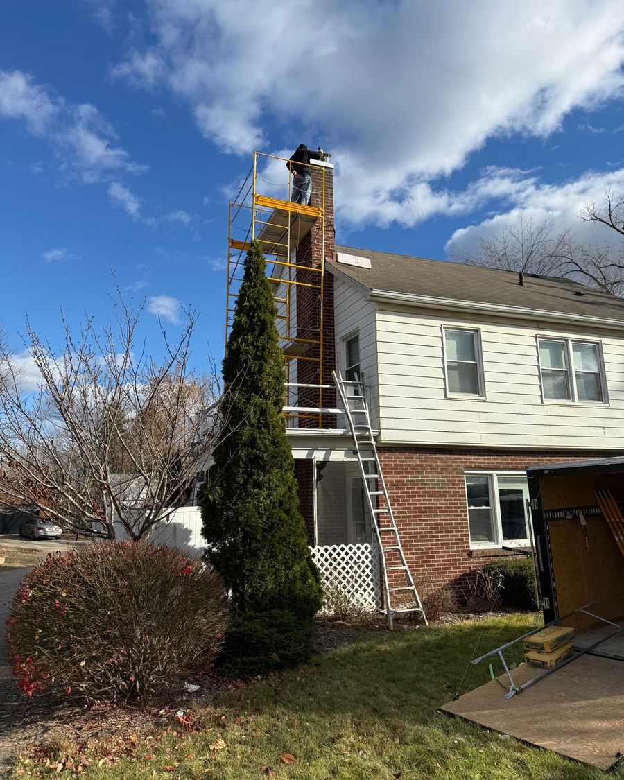Yellow scaffolding built up the side of a tall red brick chimney on a two-story house