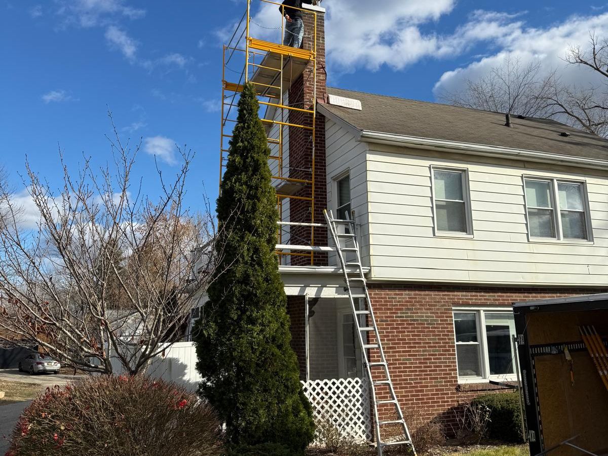 Yellow scaffolding built up the side of a tall red brick chimney on a two-story house