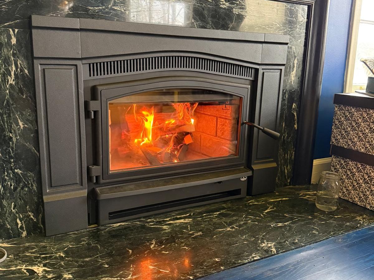 Wood-burning fireplace insert with a bright fire behind the glass door, set in a dark green marble surround under a black mantel
