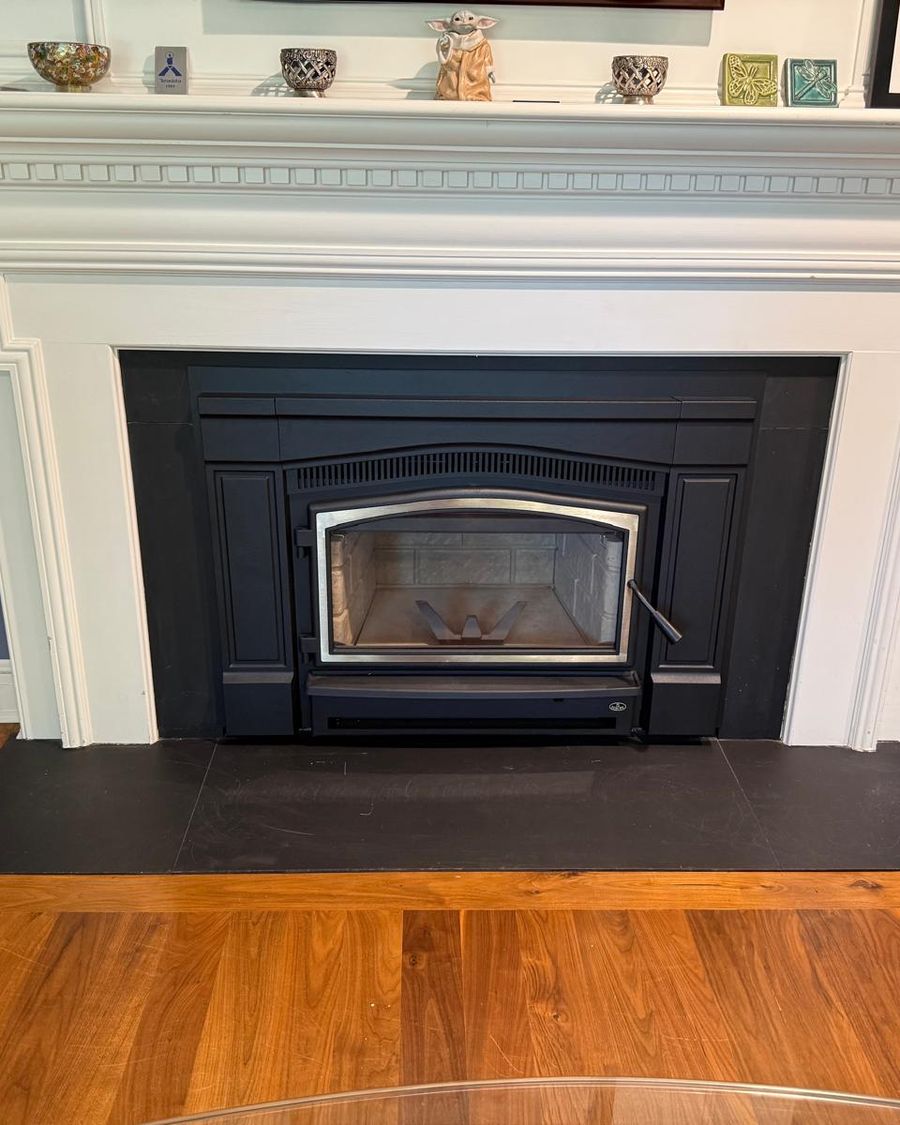 Black wood-burning insert with nickel door trim in a white mantel above a slate hearth