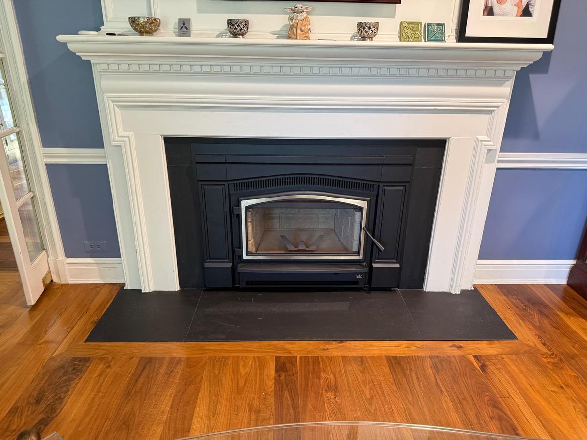 Black wood-burning insert with nickel door trim in a white mantel above a slate hearth