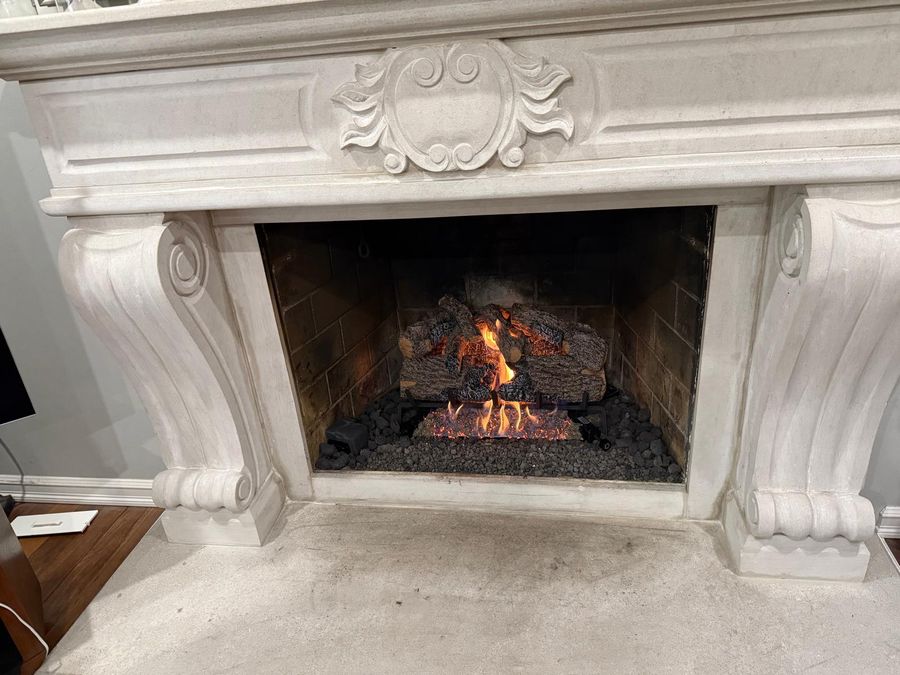 Gas log set burning over lava rock inside a fireplace framed by a carved stone mantel