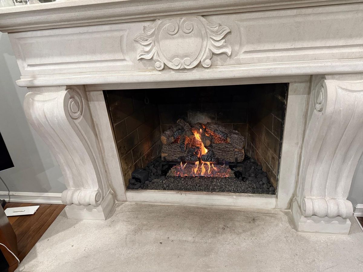 Gas log set burning over lava rock inside a fireplace framed by a carved stone mantel