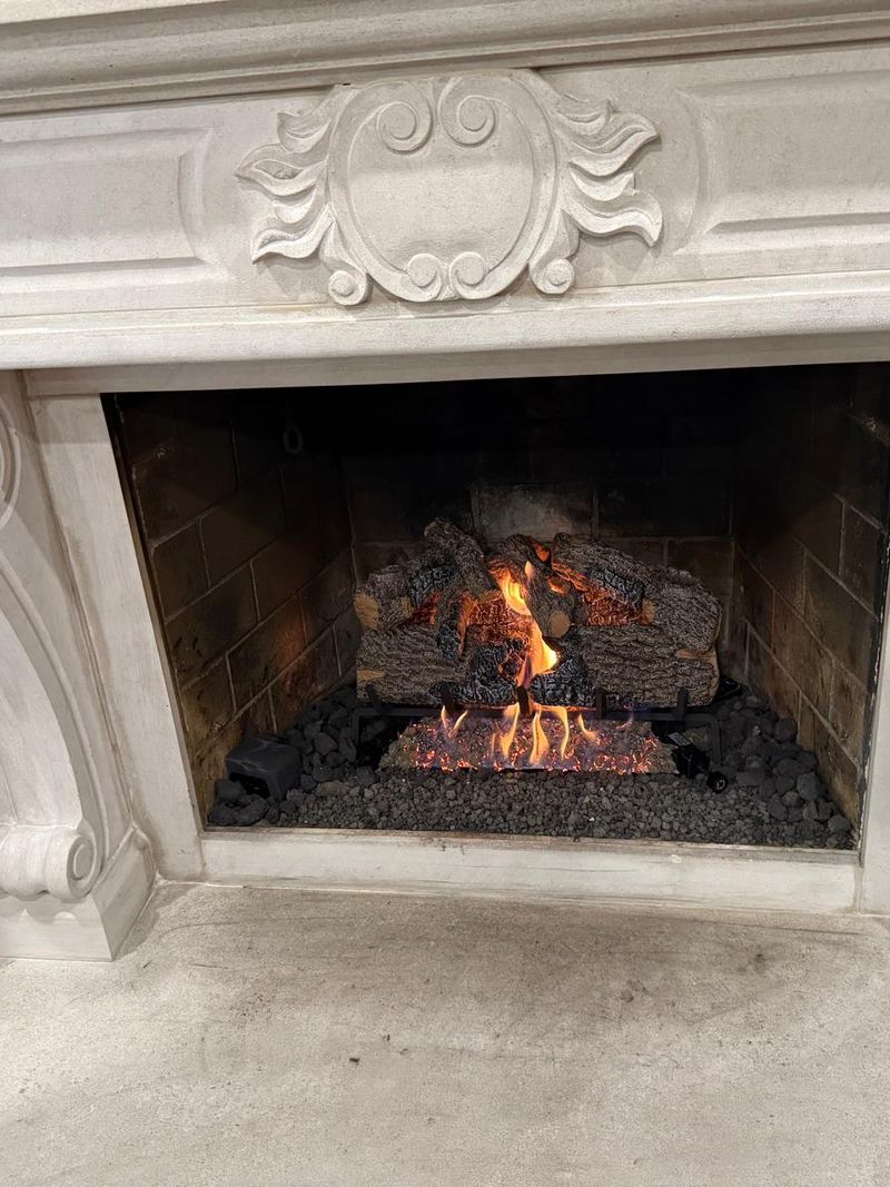 Gas log set burning over lava rock inside a fireplace framed by a carved stone mantel with scroll corbels