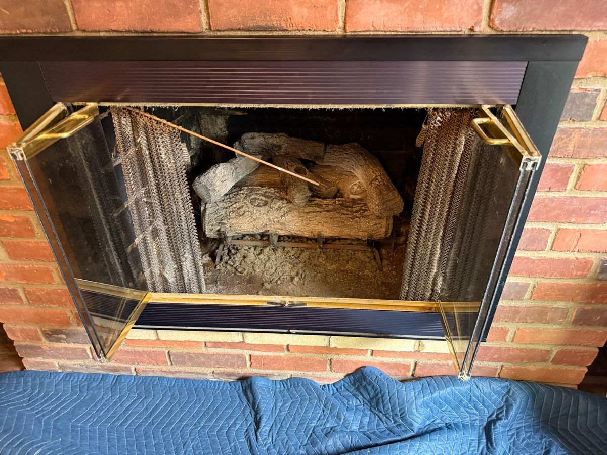 Red brick fireplace with open bifold glass doors, mesh screens and an old, dusty gas log set sitting in ash