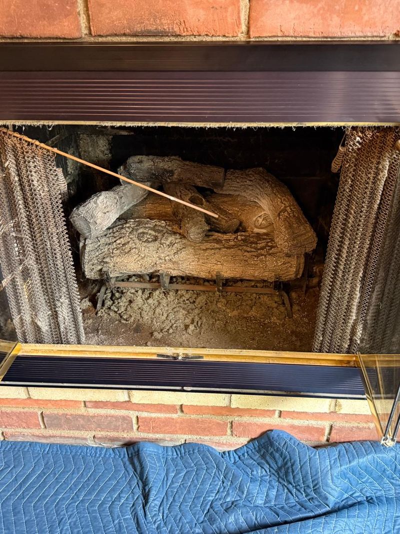 Red brick fireplace with open bifold glass doors and an old, dusty gas log set
