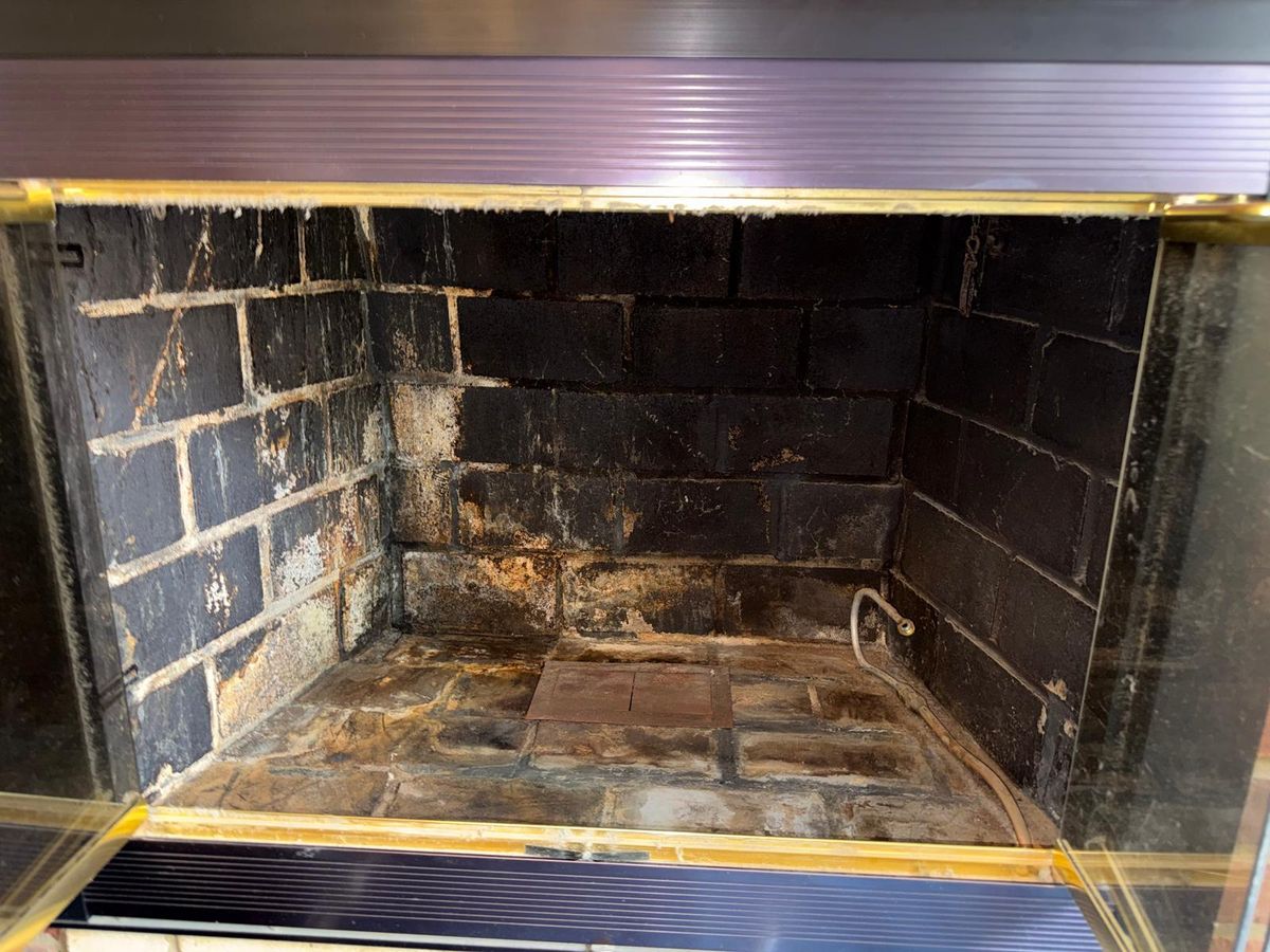 Empty masonry firebox with sooty firebrick behind open glass fireplace doors
