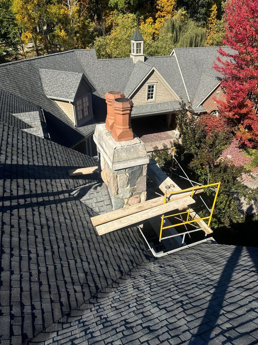 Fieldstone chimney with two terra cotta chimney pots beside a large house and autumn trees