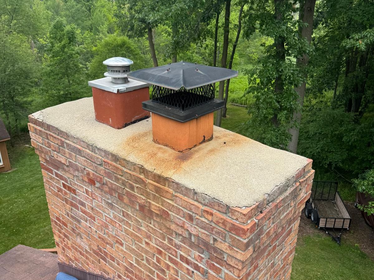 Brick chimney with a weathered concrete crown stained with rust around a black mesh cap and a stainless flue cap