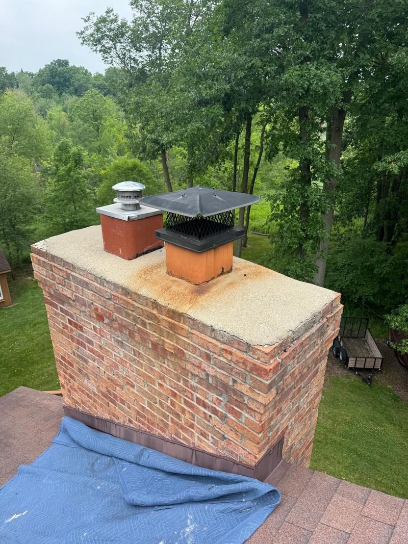 Red brick chimney with a rust-stained, weathered crown and two clay flues, one with a black mesh cap