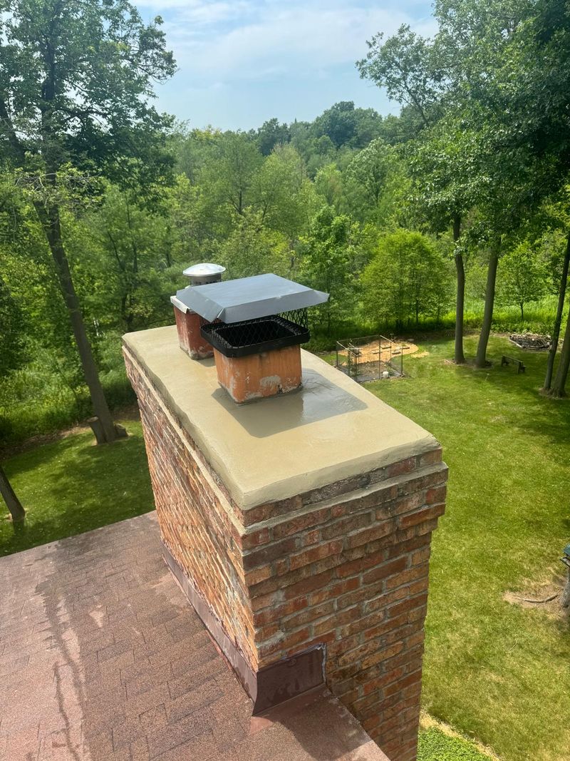The same red brick chimney with a smooth mortar crown and its black mesh cap back on