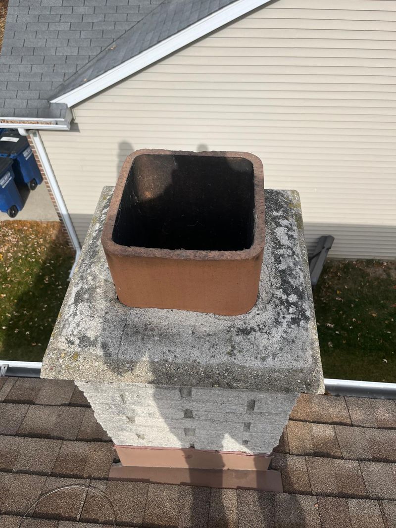 Split-face block chimney with a lichen-stained, weathered crown and an uncapped square clay flue