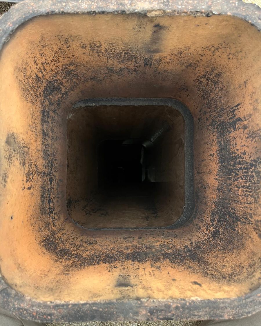 View down a square clay flue liner with orange walls streaked with soot