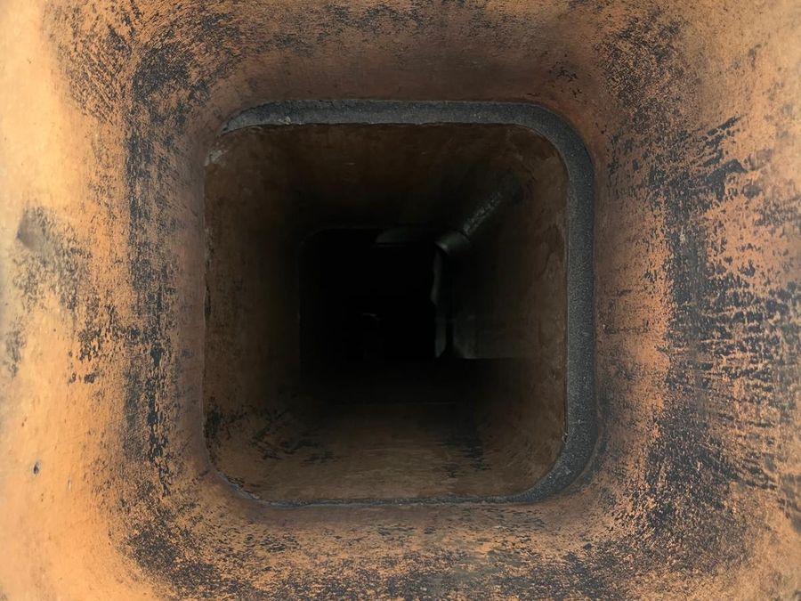 View down a square clay flue liner with orange walls streaked with soot