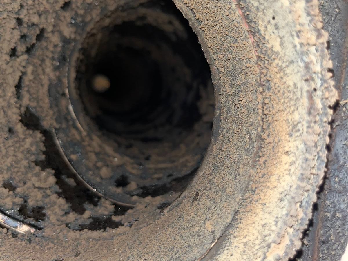 Round metal flue pipe crusted with flaky deposits on its inside walls