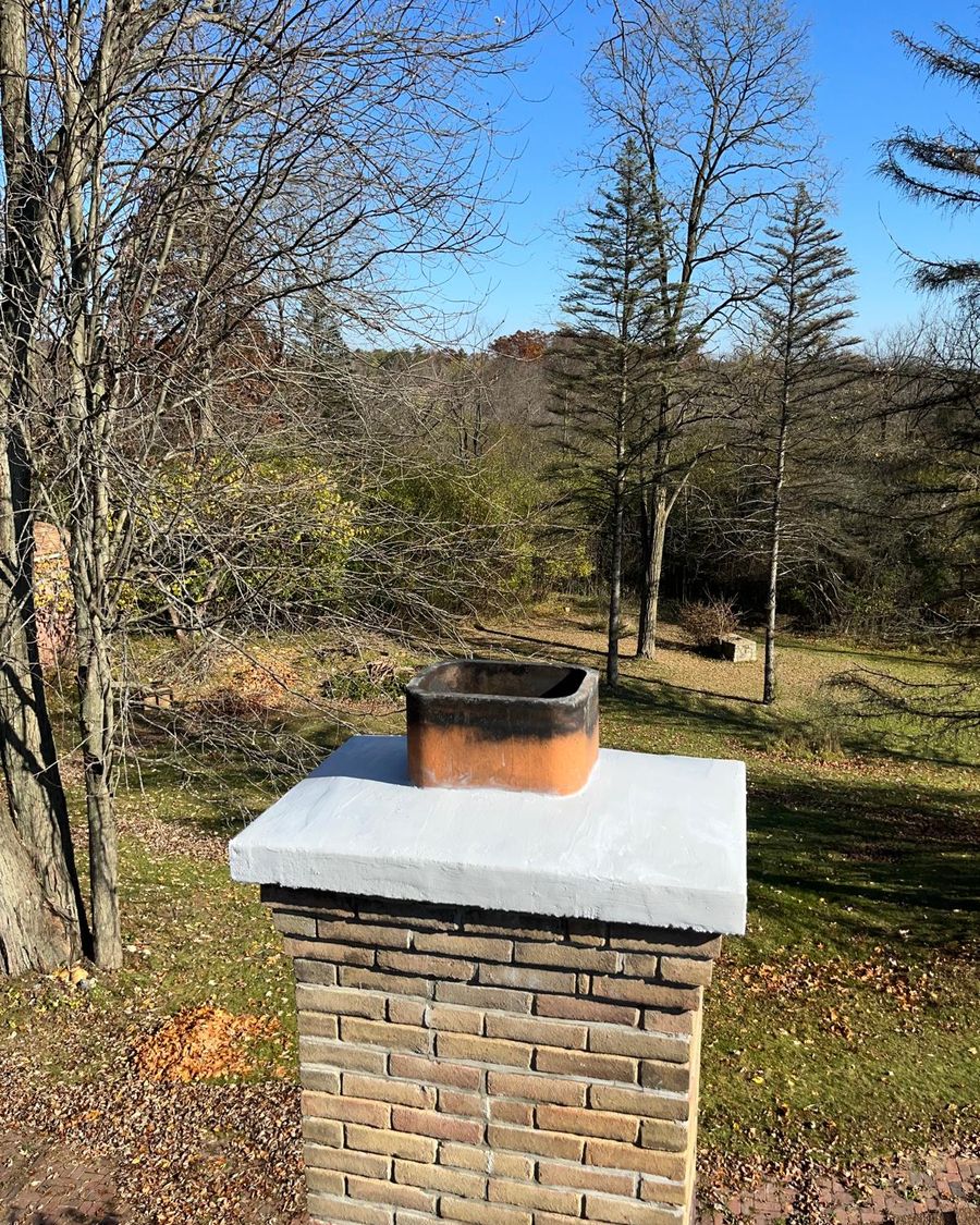 Tan brick chimney with a newly coated crown around a clay flue tile