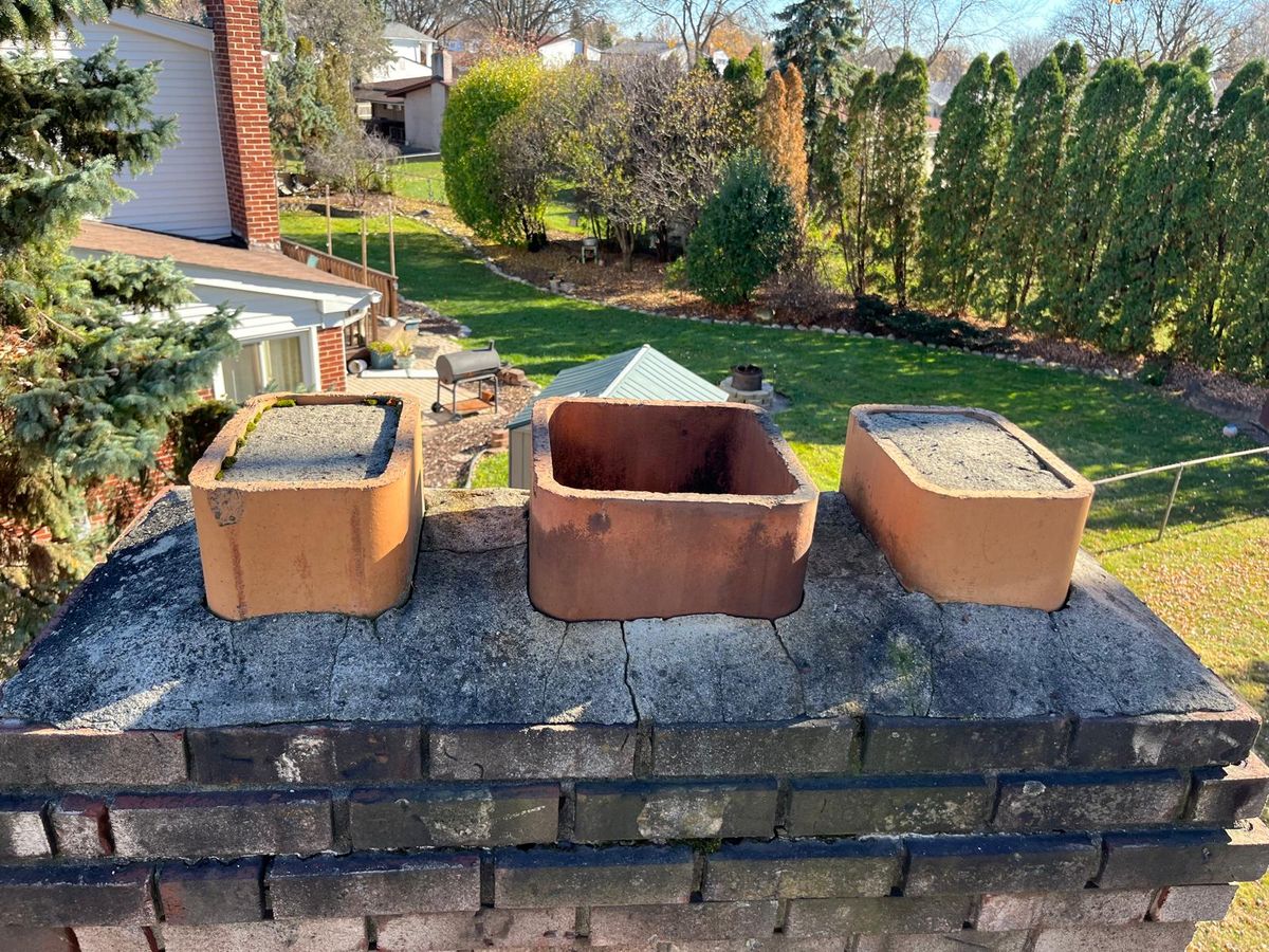 Three clay flue tiles, two of them filled in with mortar, set in a cracked and weathered crown on top of a dark brick chimney