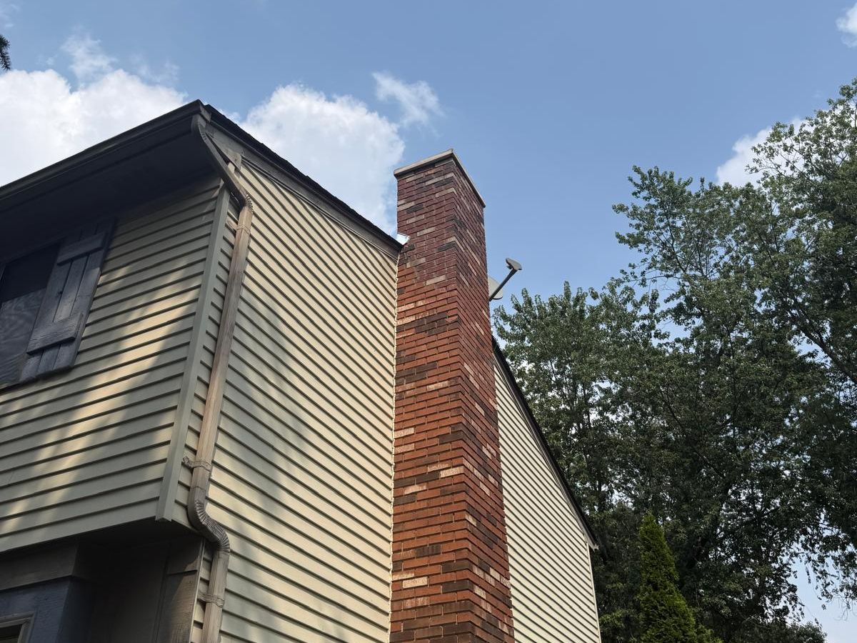 Tall blended red brick chimney rising above a sided house under a blue sky