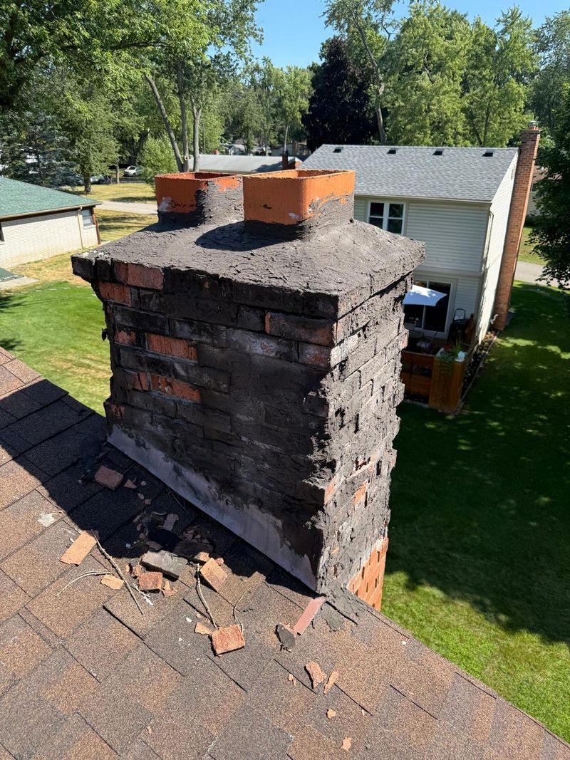 Brick chimney smeared with black tar, with broken brick pieces on the roof