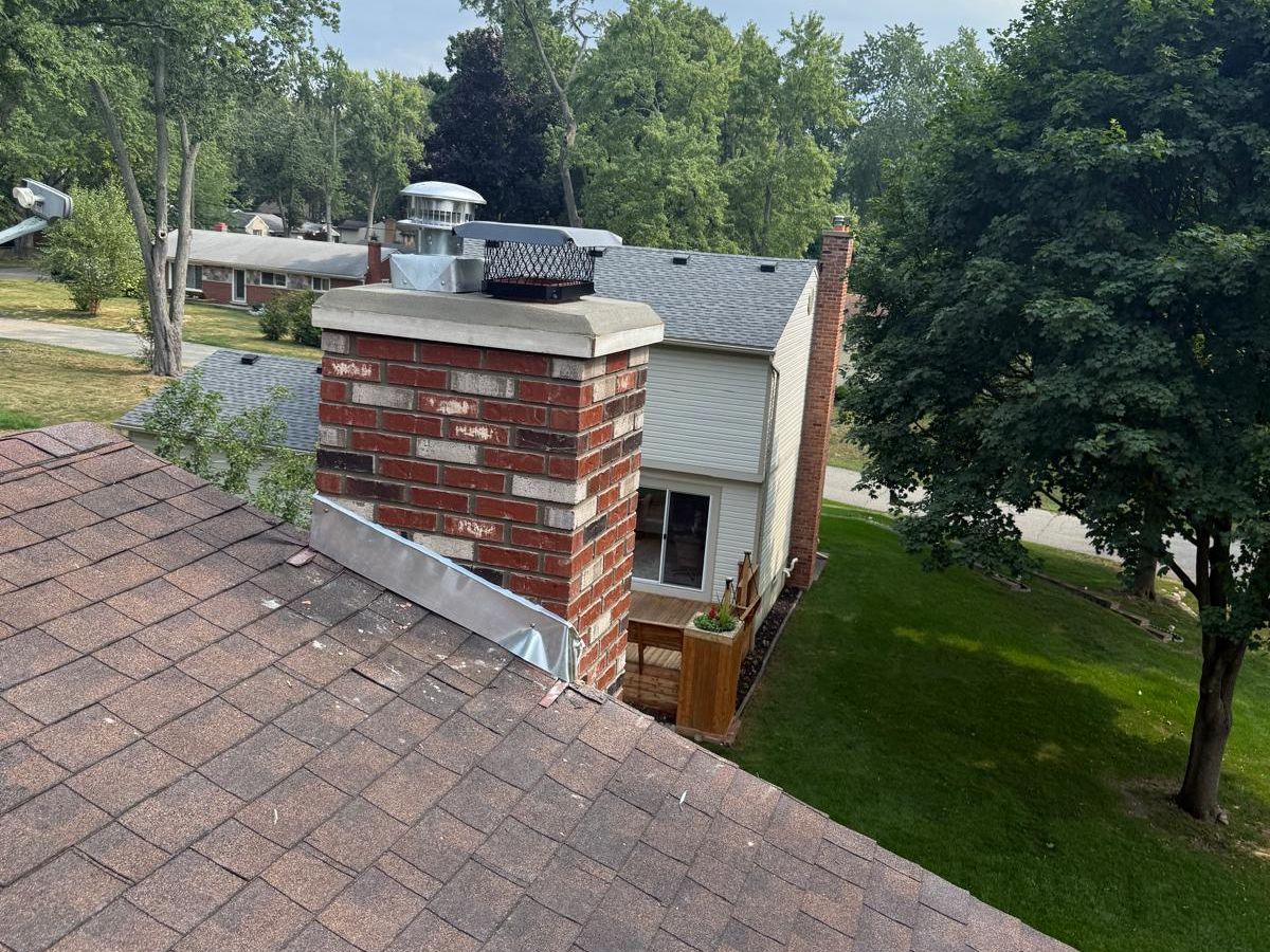 Rebuilt red and cream brick chimney with two flue caps and aluminum flashing on a brown shingle roof
