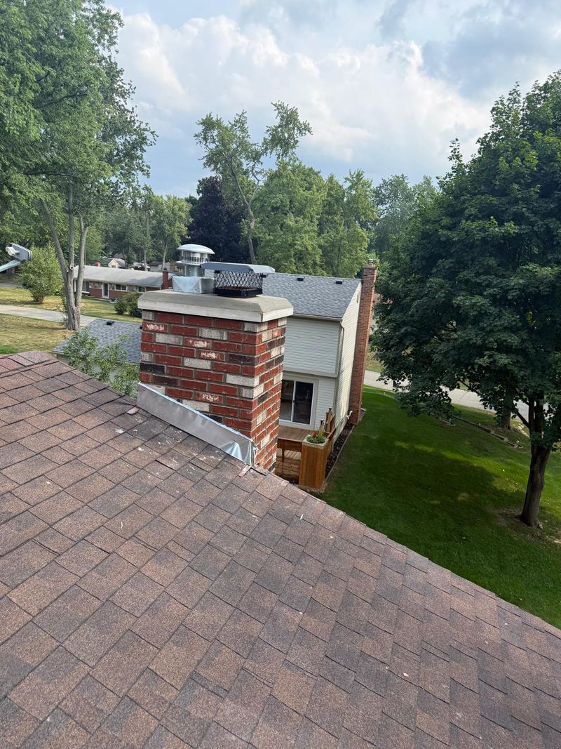 Rebuilt red and cream brick chimney with two flue caps and aluminum flashing on a brown shingle roof