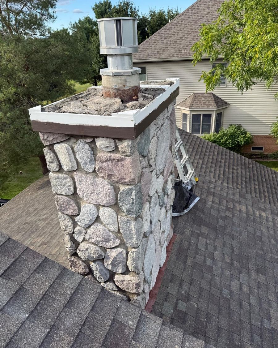 Fieldstone chimney with forms set around its top and a ladder on the roof