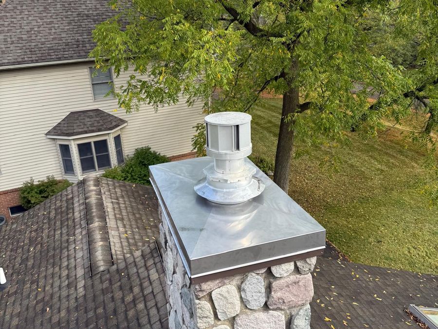 Fieldstone chimney with a new stainless steel cover and cap on a shingle roof