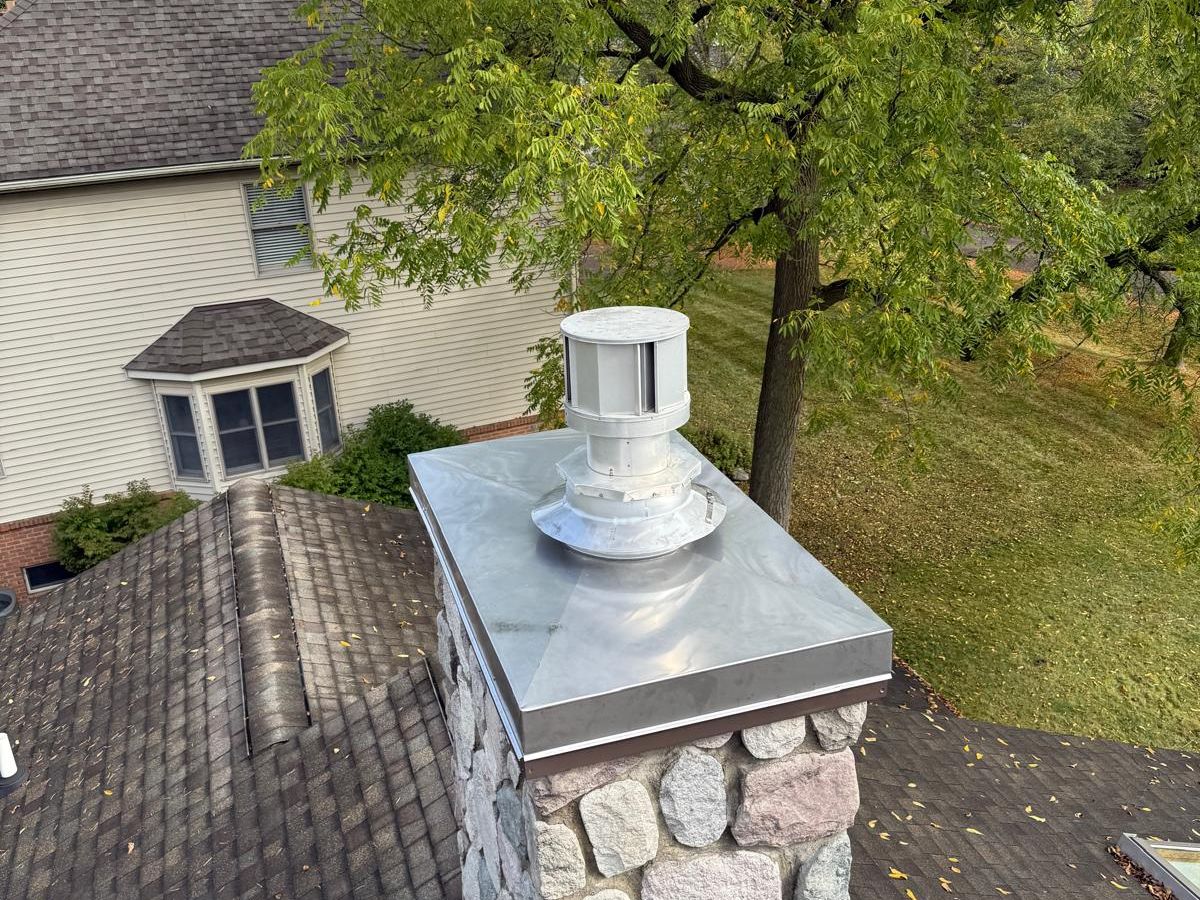 Fieldstone chimney with a new stainless steel cover and cap on a shingle roof