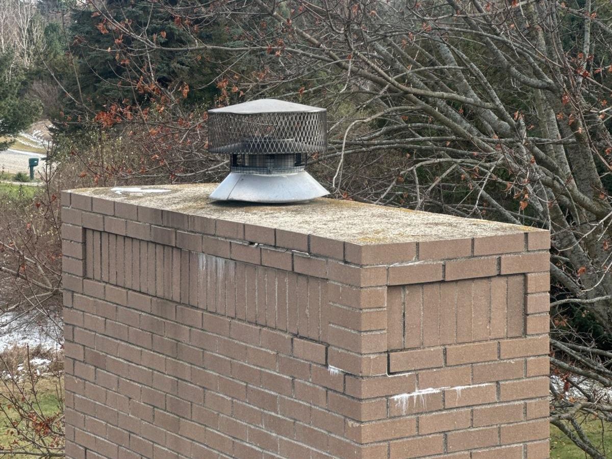 Tan brick chimney with displaced corner bricks, horizontal cracks and a small round flue cap