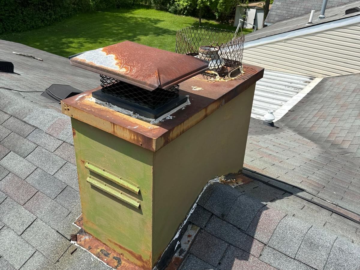 Metal chimney chase with side louvers, a rusted top and corroded base flashing