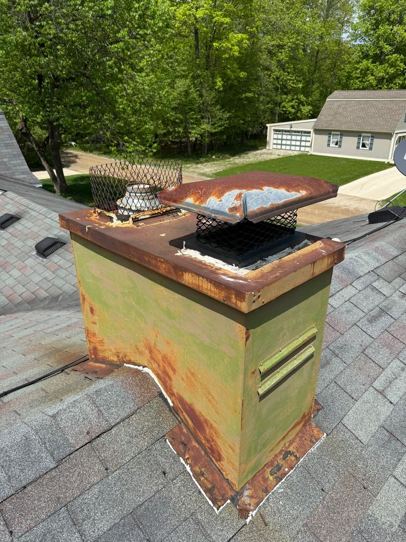 Rusted chase cover and chimney cap on a green metal chimney chase