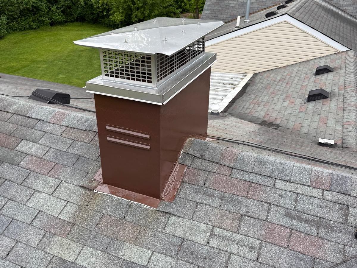 Chimney chase painted brown with a new stainless chase cover and cap on a shingle roof