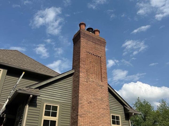 Tall brick chimney with a recessed panel and clay chimney pots on a large green-sided house