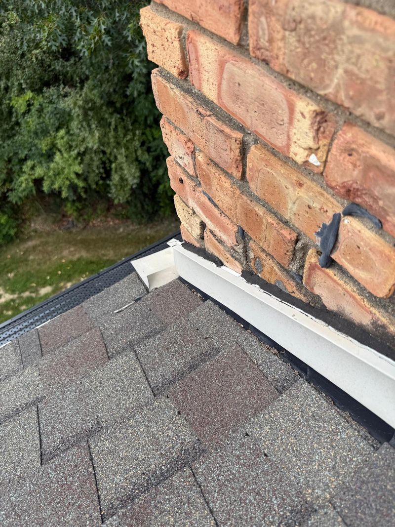Base of a brick chimney where beige step flashing meets the roof edge