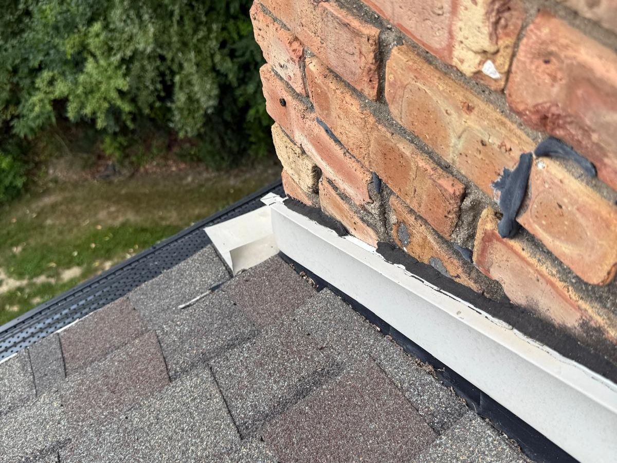 Base of a brick chimney where beige step flashing meets the roof edge