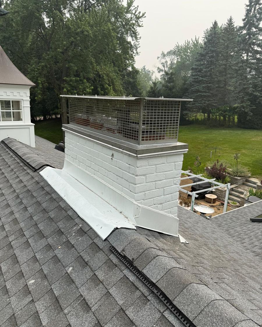 White painted brick chimney with a large stainless steel multi-flue cap beside a cupola