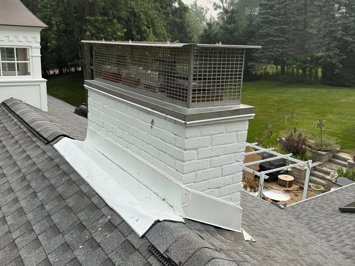 White painted brick chimney with a large stainless steel multi-flue cap beside a cupola