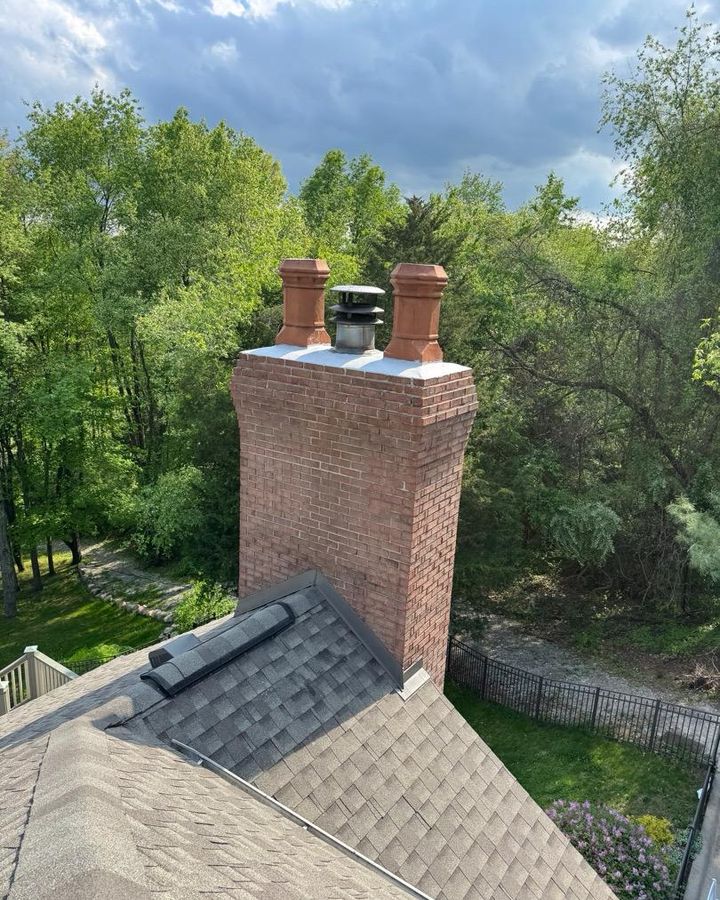 Brick chimney with two clay chimney pots and a metal flue cap above a wooded backyard