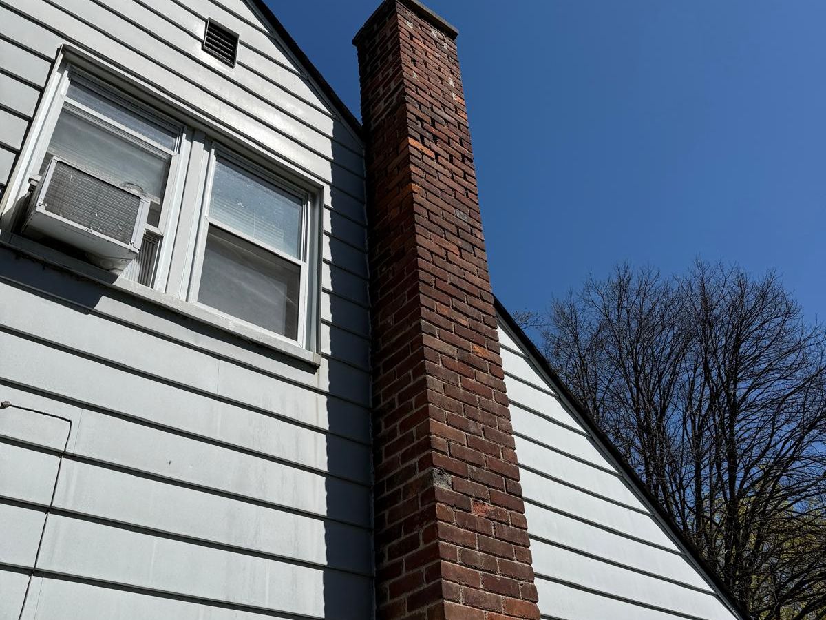 Tall brick chimney rising between two white-sided gables under a deep blue sky