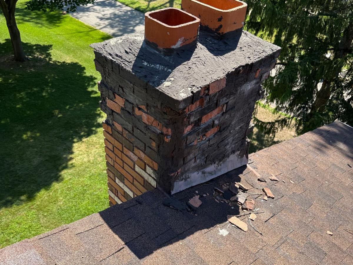 Brick chimney with crumbling brick and tar smeared over the crown and upper courses