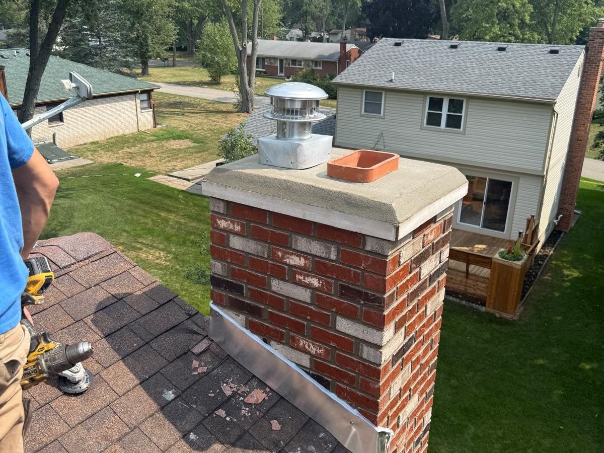 New metal flashing being fastened where a rebuilt brick chimney meets the roof, with the crown and cap above